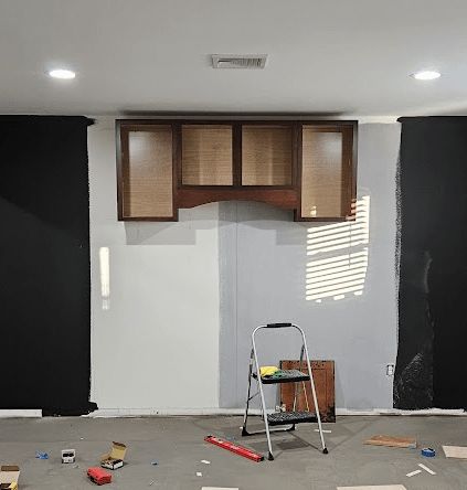 Vegg med overskap, delvis malt i hvitt og svart, med grått gulv og stige